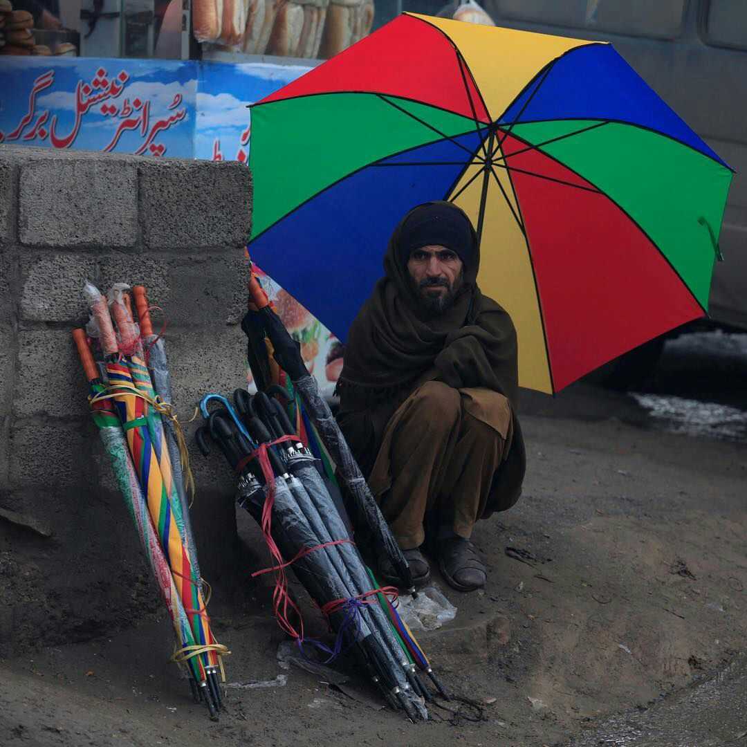 pakistan, 一个男子在雨中卖伞 他蹲在那里面无表情 他应该也是因为