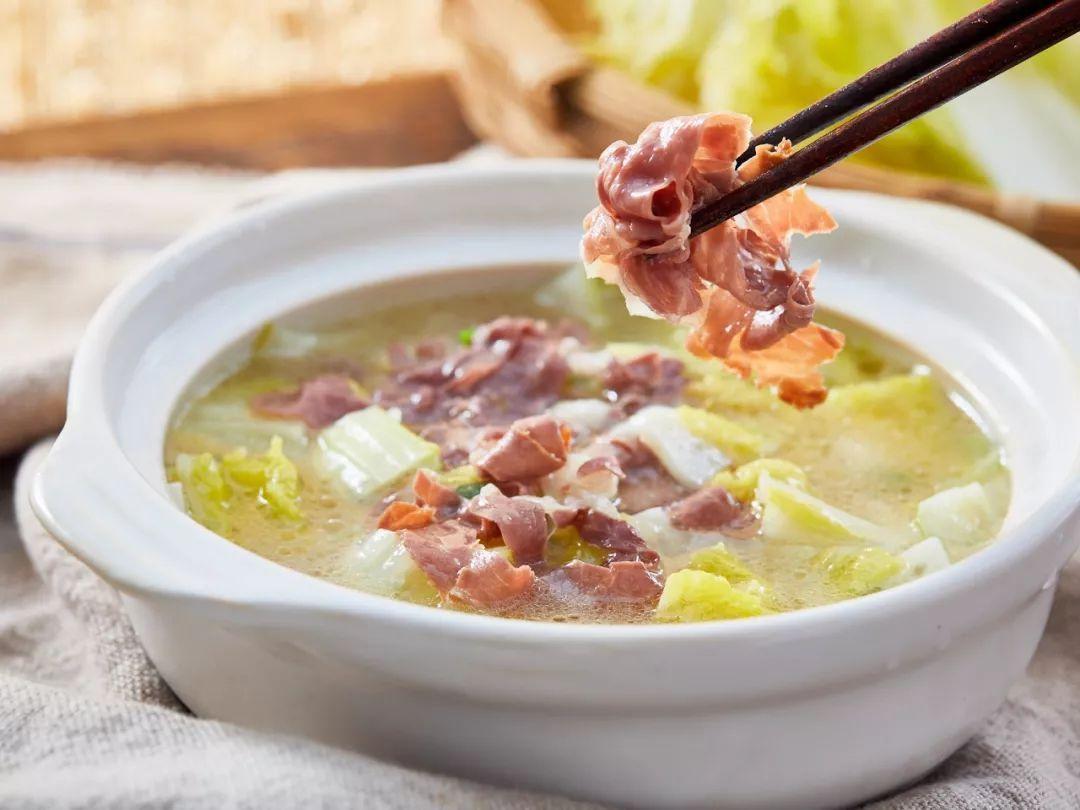 将切好的火腿片和两三叶白菜放入烧开的热汤中,蔬菜的清香混合着火腿